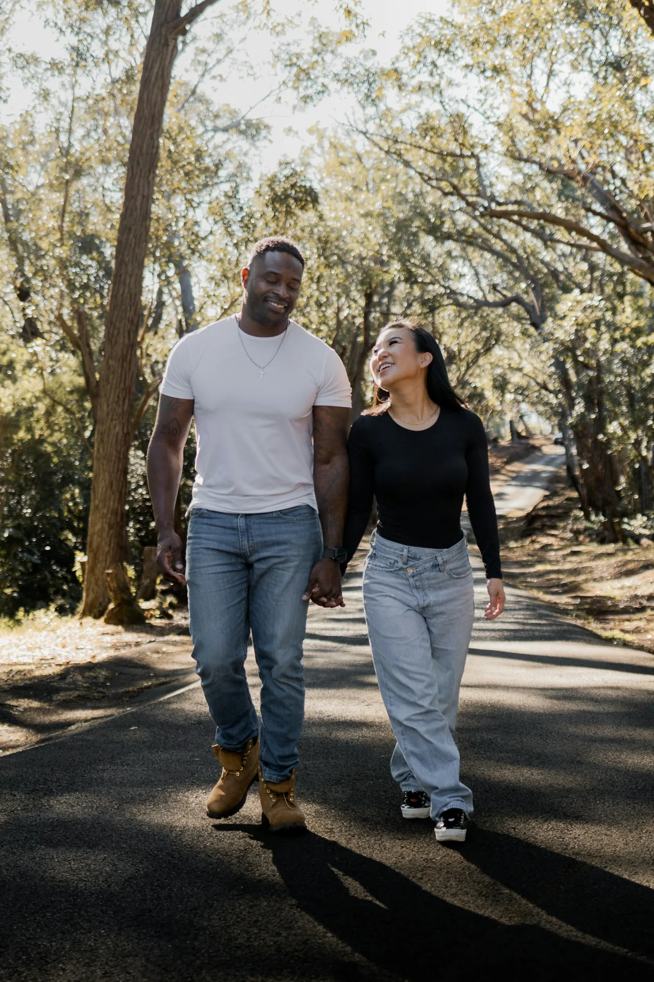 A couple holding hands and smiling during a walk beneath the trees